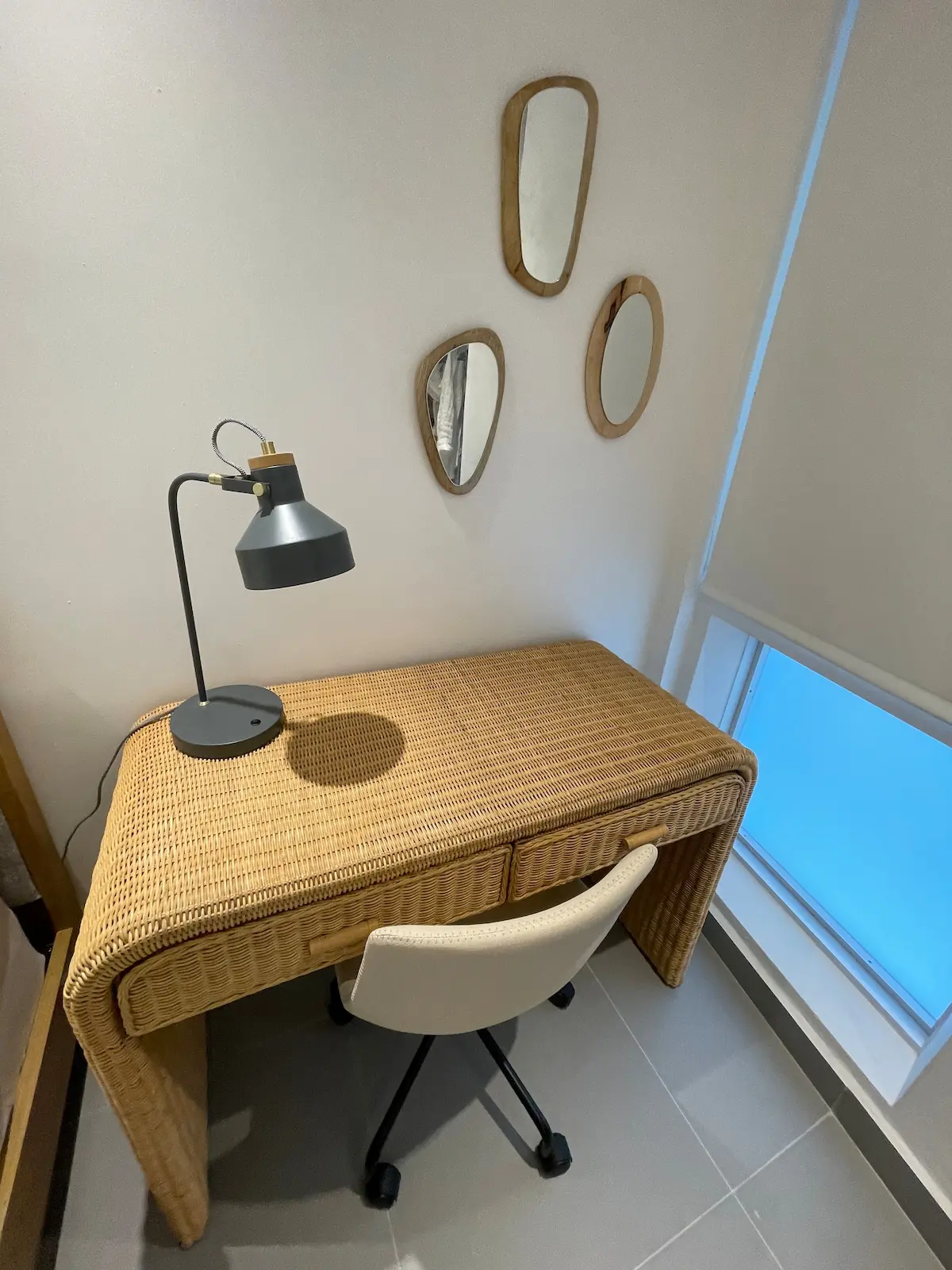 Dedicated workspace with a woven desk, a black task lamp and a rolling chair beside a window.